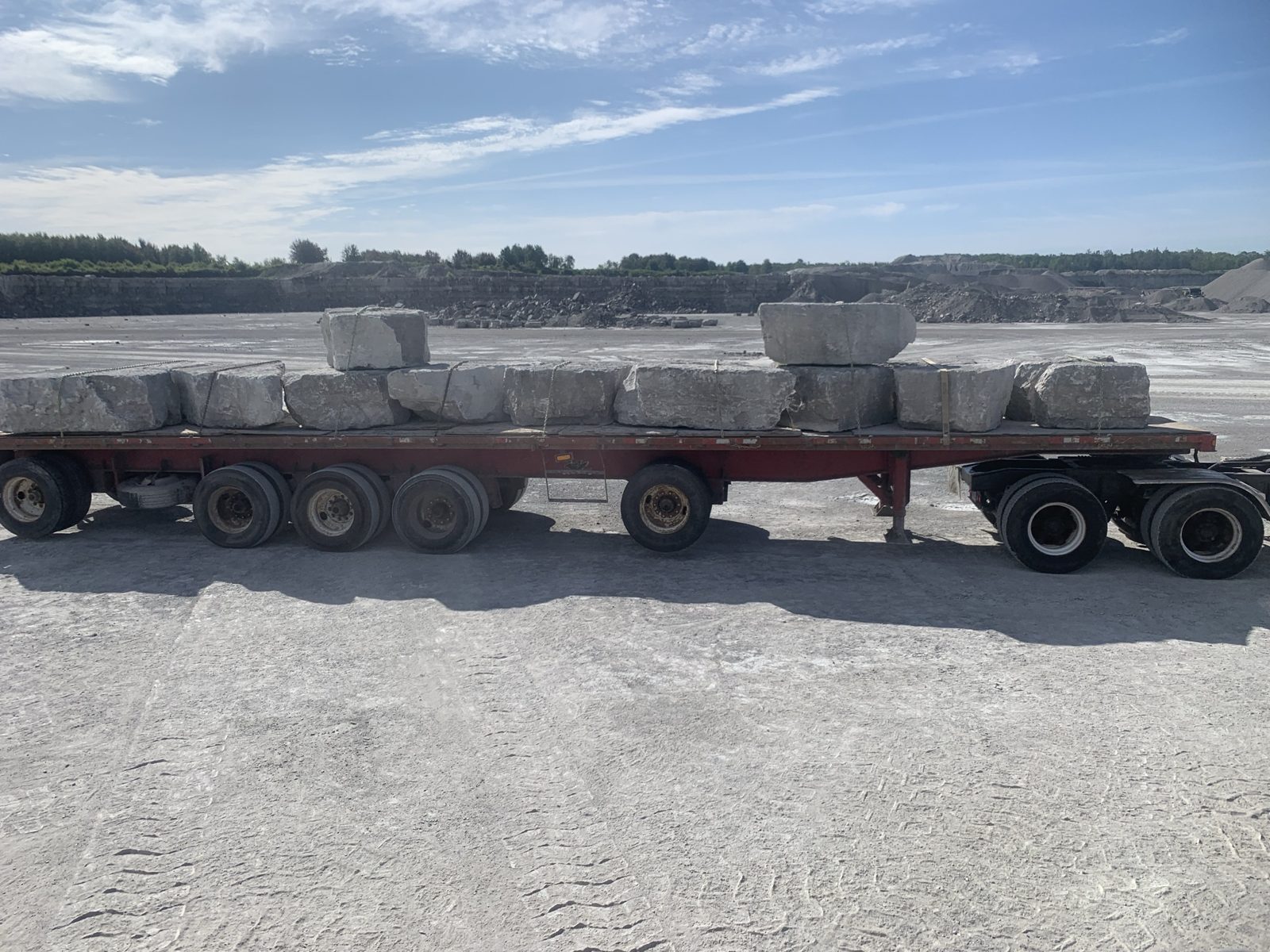 Large armour stone blocks strapped on a flatbed trailer at the quarry, ready for delivery